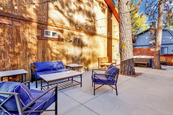 An outdoor seating area with tables and chairs, a wooden wall, and string lights.