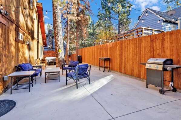A backyard with a wooden fence, outdoor furniture, and a barbecue grill.