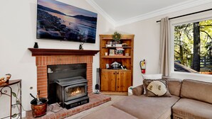 Una sala de estar con chimenea, televisor montado en la pared, estantería de madera y ventana con vistas a árboles.