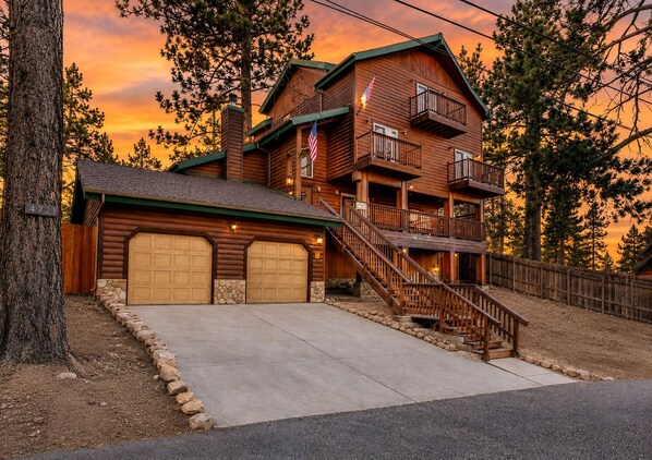 A two-story log cabin with a stone foundation, a front garage, and a staircase leading to the upper level.