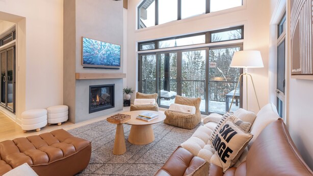 Ein geräumiges Wohnzimmer mit Kamin, großen Fenstern und hoher Decke.