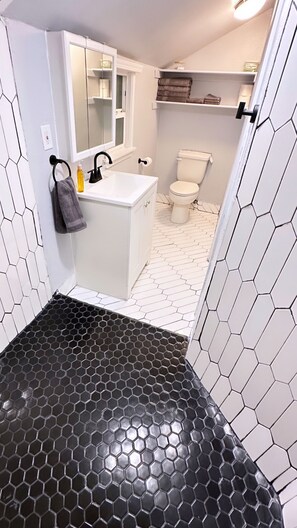 A bathroom with a white sink, mirror, and toilet. The floor has a black and white hexagonal tile pattern. - The Oasis - Your Luxury 2BR/1.5BA Home in Downtown Modesto (Modesto)