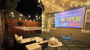 Un patio trasero con una hamaca, una mesita y una pantalla para proyector mostrando un menú.