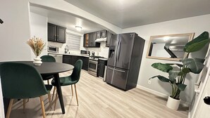 Una cocina moderna con armarios oscuros, un refrigerador de acero inoxidable y una zona de comedor con mesa y sillas.