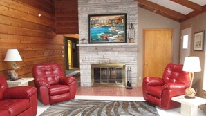 A cozy living room with two red leather chairs, a fireplace, and a painting of a harbor scene.