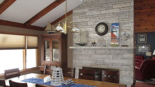 A dining area with a wooden table, chairs, and a decorative centerpiece. There is a fireplace with a clock and wall art above it.