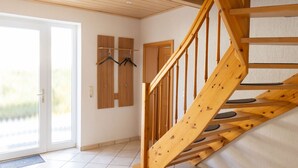 Un escalier en bois avec une rampe, une porte dotée d’un panneau de verre et un porte-manteau mural avec des cintres.