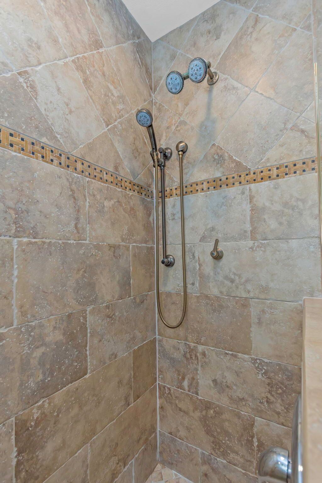 A shower with a handheld showerhead and a fixed showerhead, both mounted on a tiled wall with a decorative border.