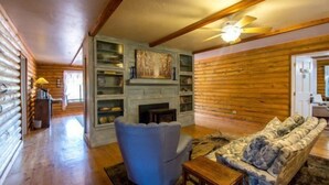 L’intérieur d’une cabane en rondins, avec une cheminée, un fauteuil bleu et un canapé à motifs de pierres.