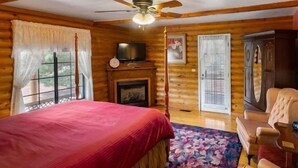 Une chambre située dans un chalet en rondins, équipée d’un lit, d’une télévision, d’une cheminée et d’un ventilateur de plafond.