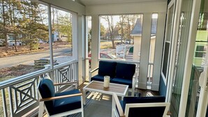 A covered porch with a wooden deck, white railings, and a seating area with a table and chairs. - Beautiful New 5 BR in Bethany West - EV Charging (Bethany Beach)