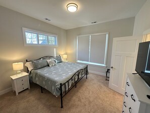 Un dormitorio con una cama, dos mesitas de noche, una lámpara, una ventana con persianas y una puerta.