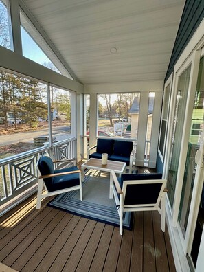 A covered porch with a wooden deck, white railings, and a seating area with a table and chairs.