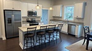 A modern kitchen with white cabinets, stainless steel appliances, a granite countertop, and a bar area with stools. - Beautiful New 5 BR in Bethany West - EV Charging (Bethany Beach)