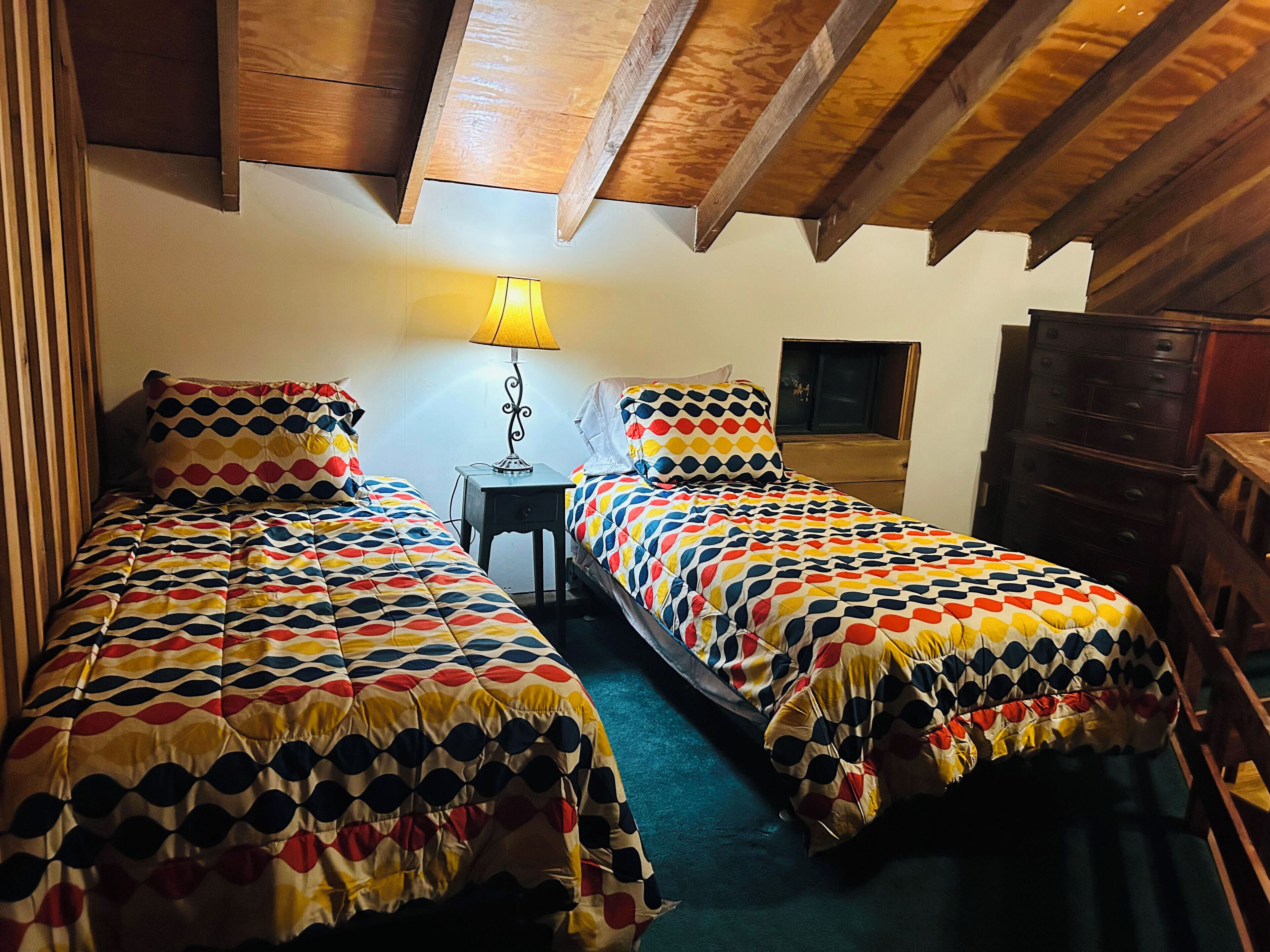 Una habitació amb dues lliteres, una tauleta de nit amb una làmpada, un armari i una finestra petita.