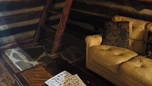 Interior de cabana rústica com escada de madeira, sofá de couro e janela.