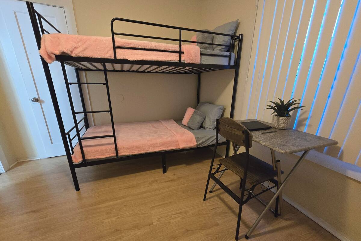 A bunk bed with a desk and chair, a potted plant, and a window with blinds.
