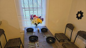 A dining table with four black bowls, a vase of flowers, and cutlery.