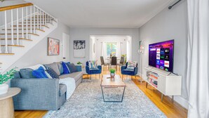 Un salon moderne avec un escalier, un canapé gris, des fauteuils bleus, une table basse et un téléviseur posé sur un meuble.