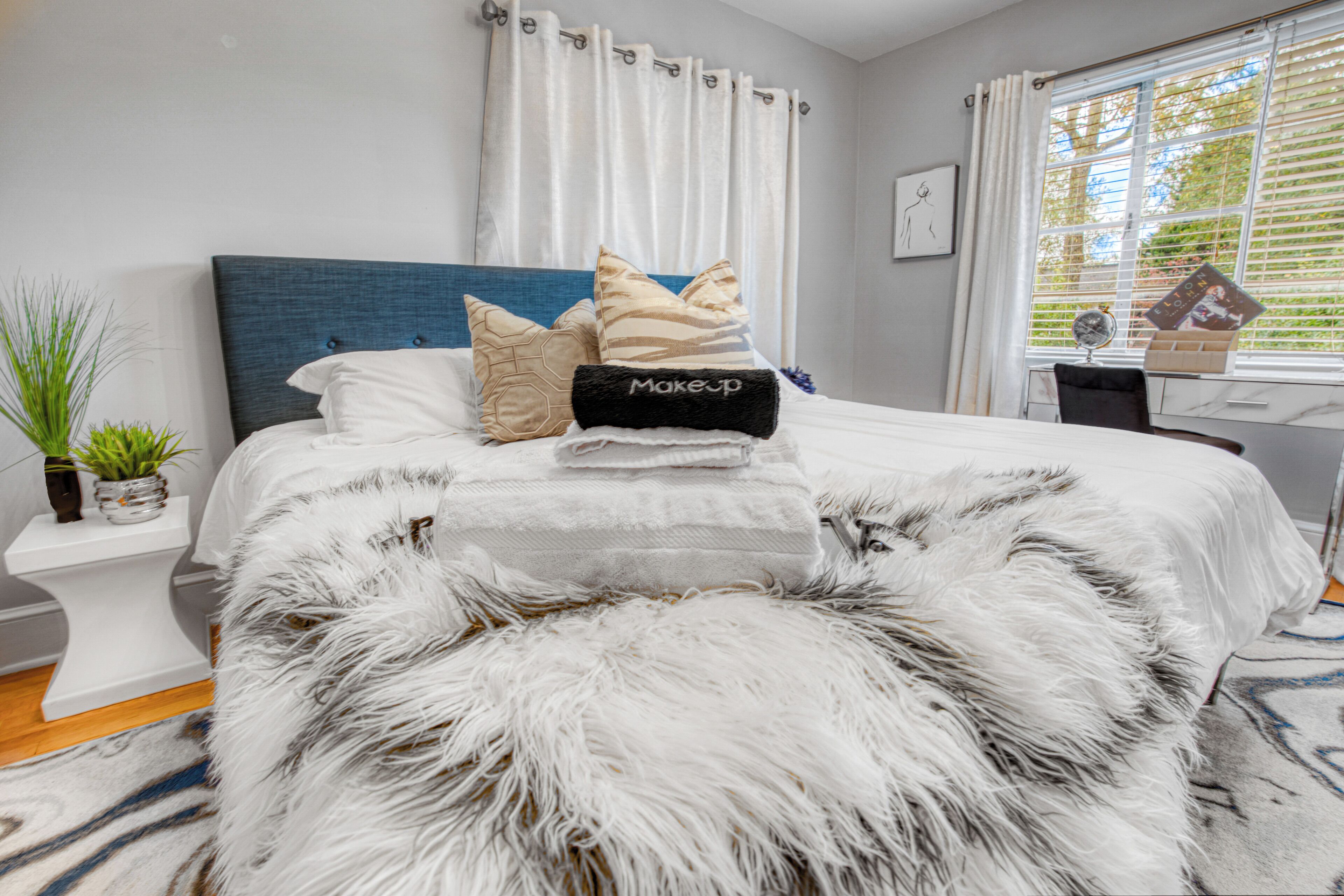 Un lit bien fait, agrémenté de coussins décoratifs, un tapis blanc moelleux et une petite table de chevet avec une plante.