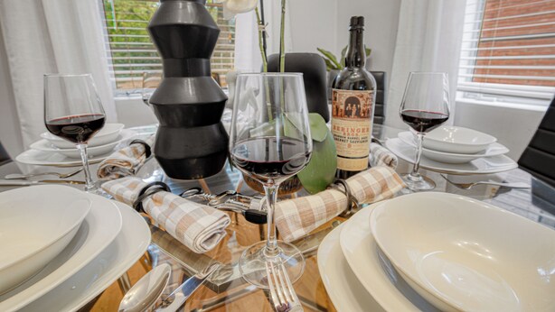 Une table à manger dressée avec des assiettes, des verres et une bouteille de vin, entourée de fleurs blanches et d’un vase noir.