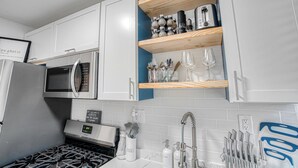 Une cuisine moderne avec des armoires blanches, un four à micro-ondes encastré, une cuisinière à gaz et des étagères en bois au-dessus de l’évier.