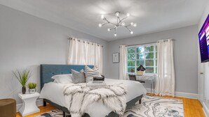 Une chambre à coucher comprenant un lit, une table de chevet, une chaise, un bureau et un téléviseur.