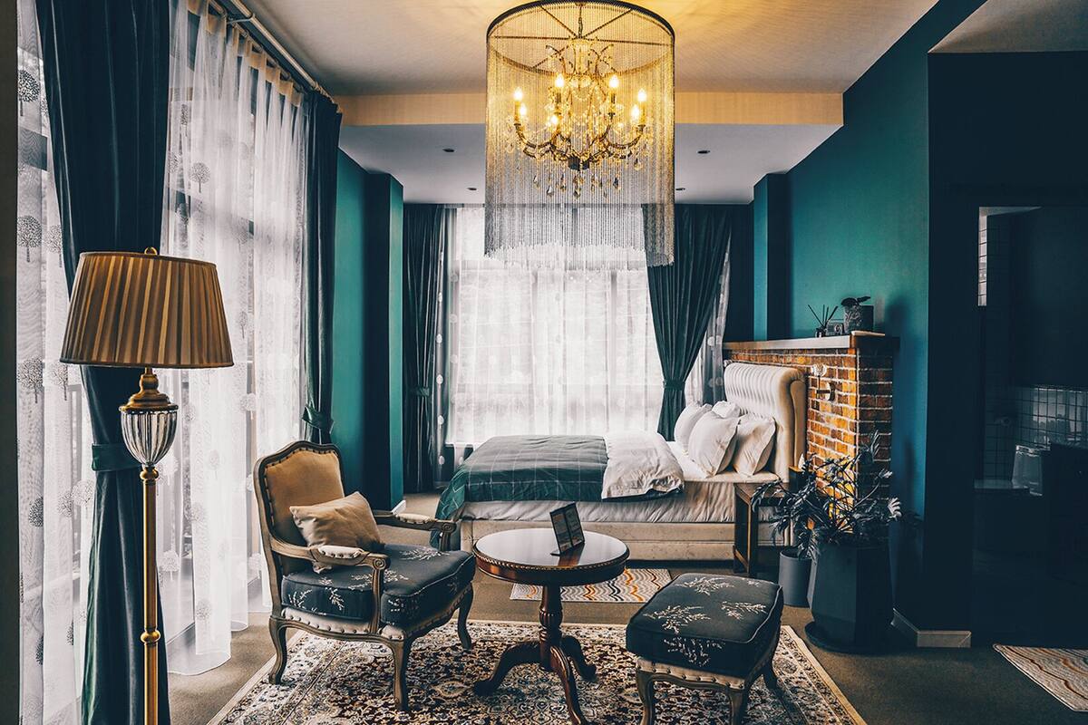 Une chambre d’hôtel avec un lit, une chaise, une table, une lampe et un lustre.