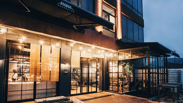 A modern building with a restaurant on the ground floor, featuring large windows and a wooden deck with outdoor seating. - sees the sea and sea view boutique B&B (Shenzhen)