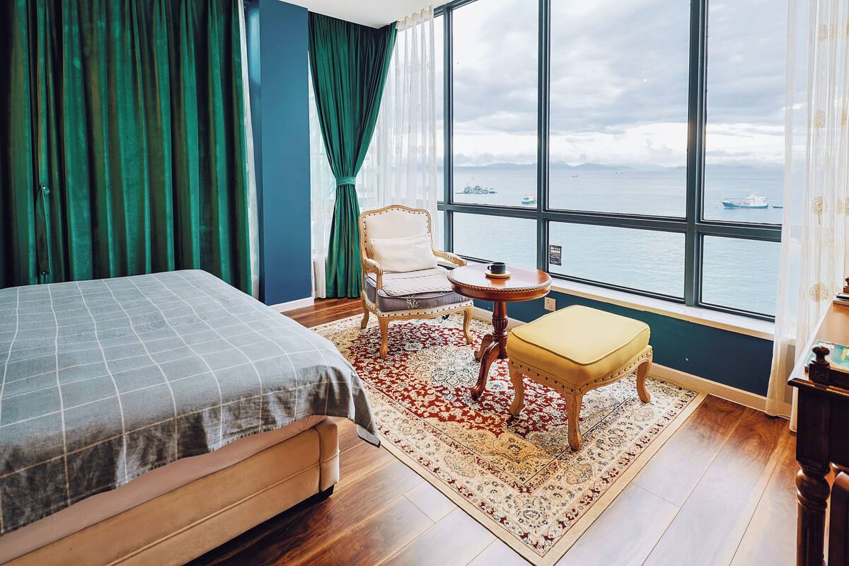 Une chambre d’hôtel avec un grand lit, une chaise, une petite table et une vue sur la mer.