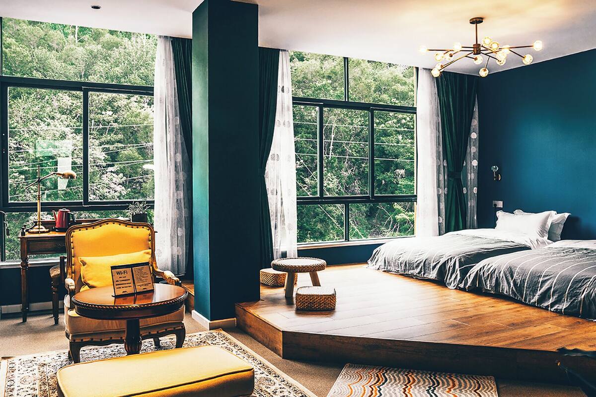 Une chambre avec une grande fenêtre, un lit, une chaise, une petite table et un tapis.
