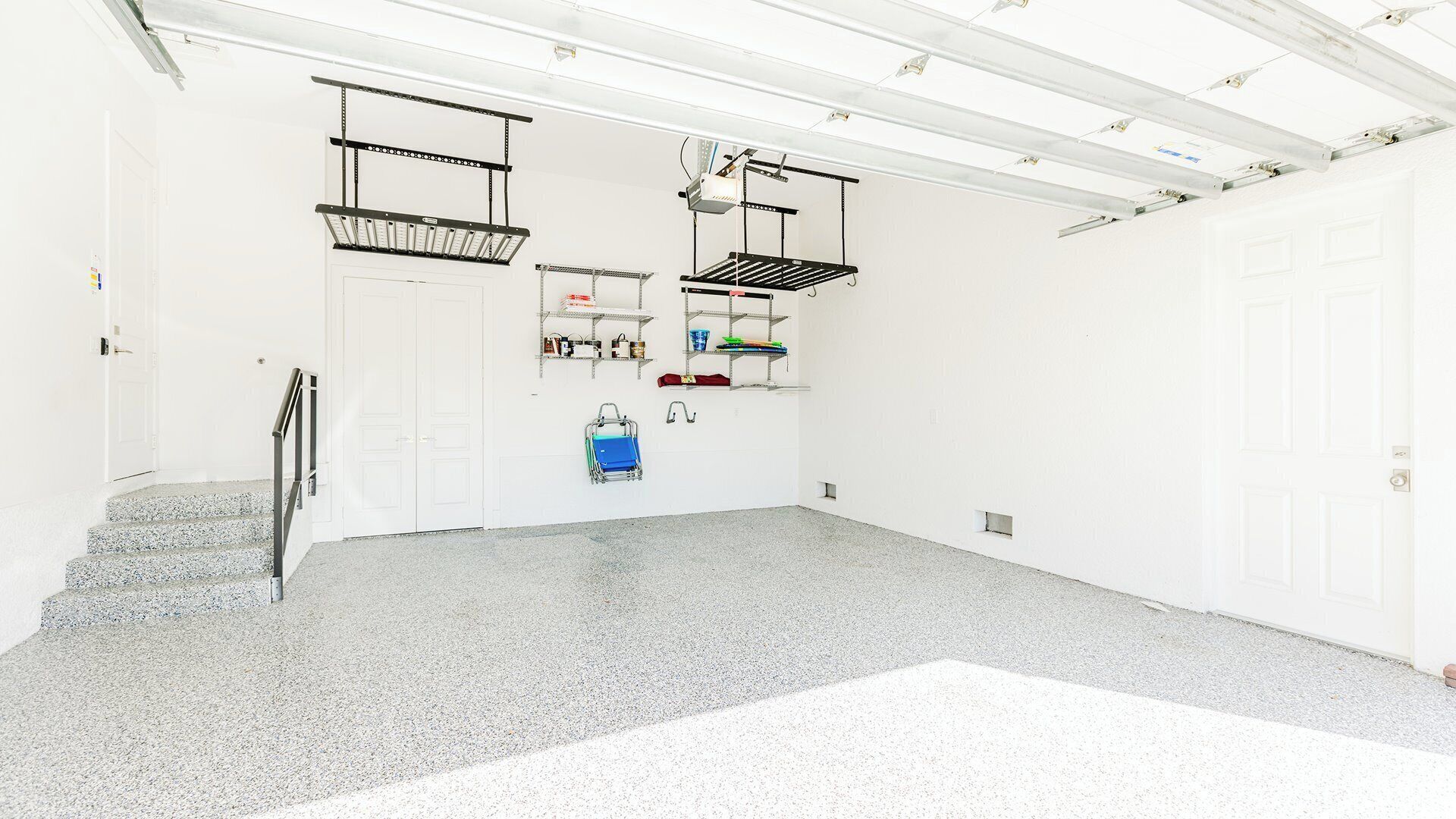 Eine saubere, gut beleuchtete Garage mit Betonboden, Metallregalen und einer Treppe zu einer Tür.