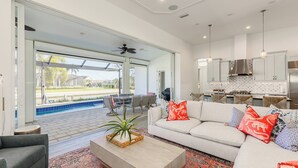 Un salon spacieux avec un grand canapé, une table basse et une vue sur une piscine et un espace repas extérieur.