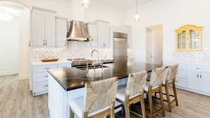 Une cuisine moderne avec des meubles blancs, un îlot central en acier inoxydable et une cuisinière intégrée.