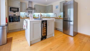 A modern kitchen with stainless steel appliances, light grey cabinetry, and a central island with a built-in oven.