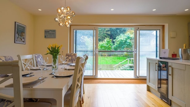 A dining area with a table set for four, a vase with flowers, and a view of a garden through large sliding doors.