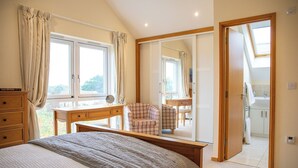 A bedroom with a bed, a desk, a chair, and a mirror. There is a bathroom visible through an open door.