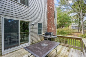 A deck with a grill and a table, a sliding glass door, and a brick chimney.