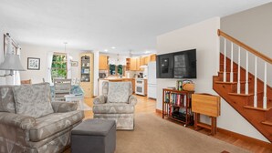 A living room with a sofa, armchair, ottoman, and a TV mounted on the wall. - Woods Edge: Walk to Red River Beach, Pet Friendly (Harwich Port)