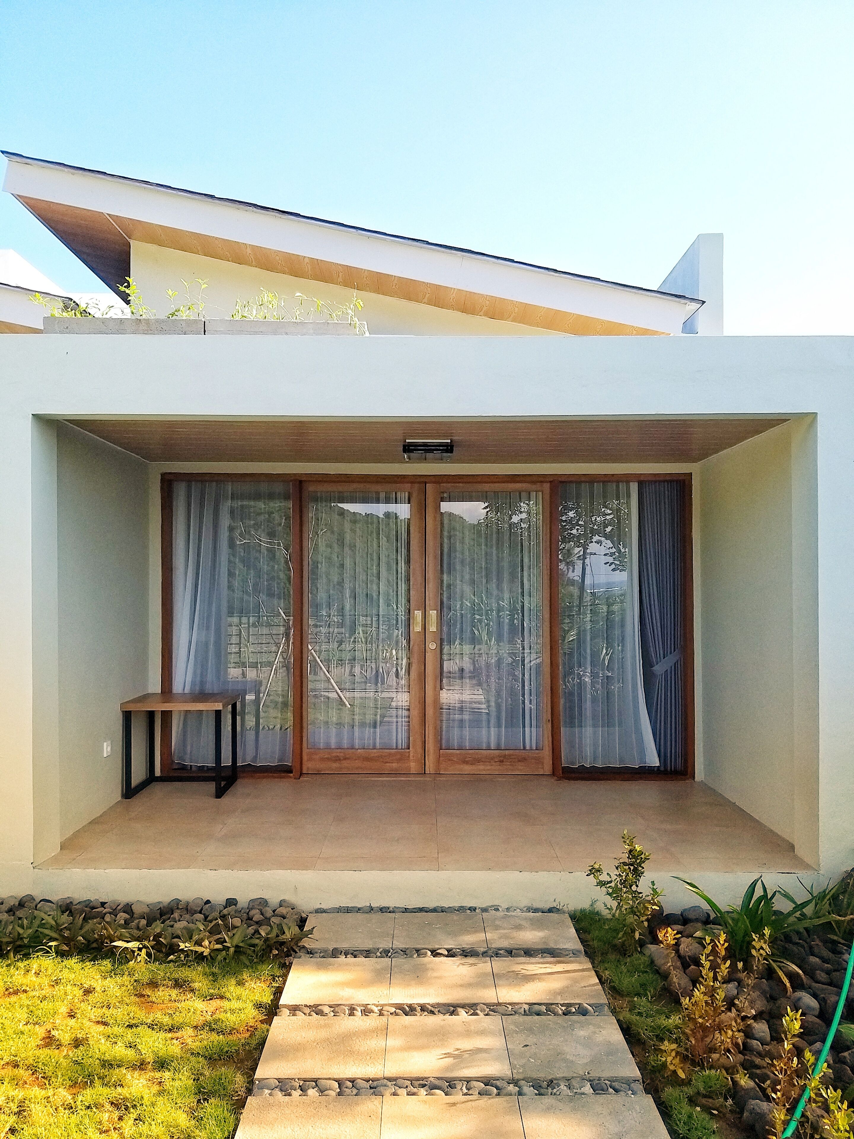 A modern house with a covered patio, a small table, and a garden with a stone pathway.