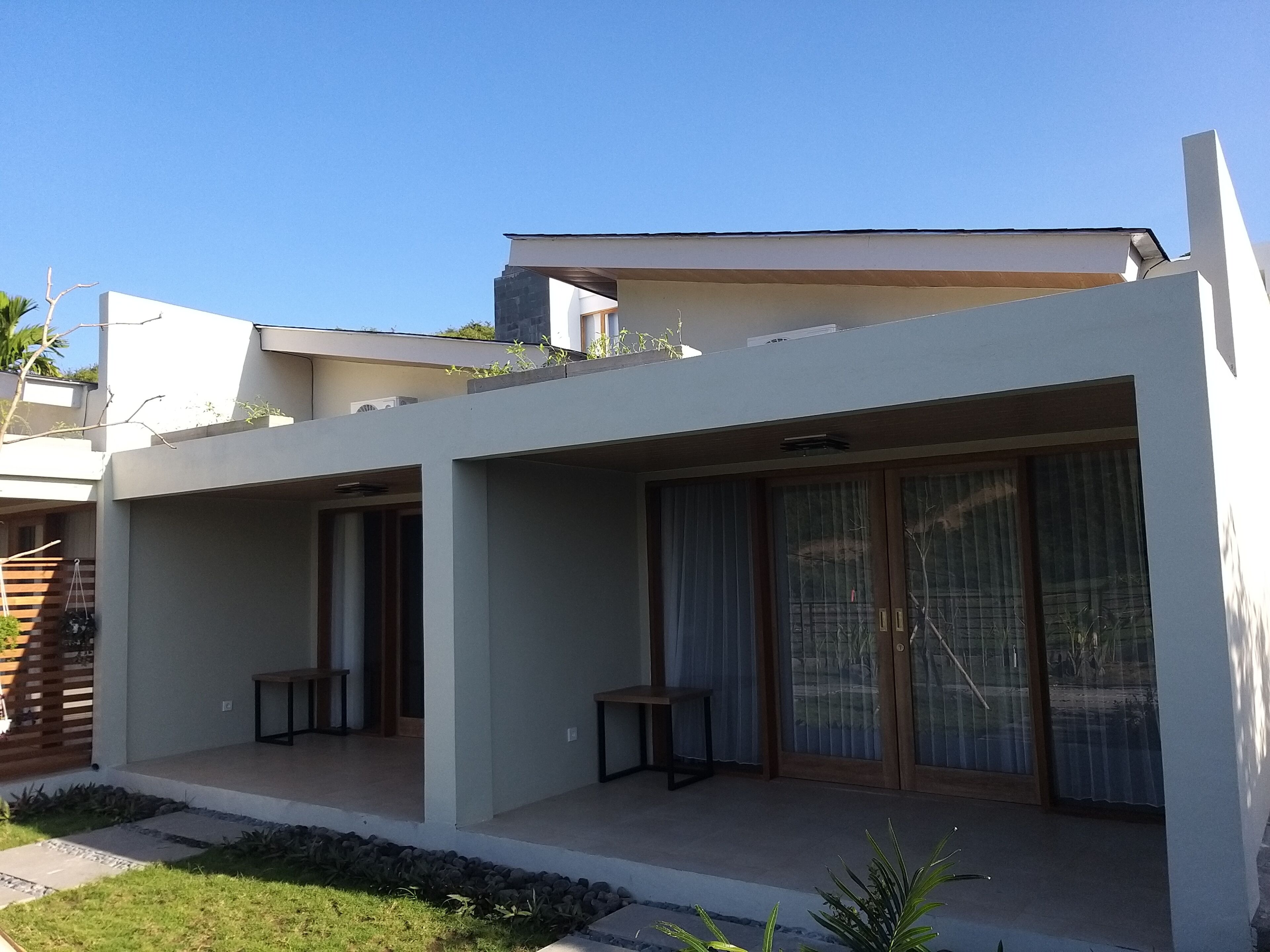 A modern two-story house with a flat roof, large sliding glass doors, and a small patio area with a table and chairs.