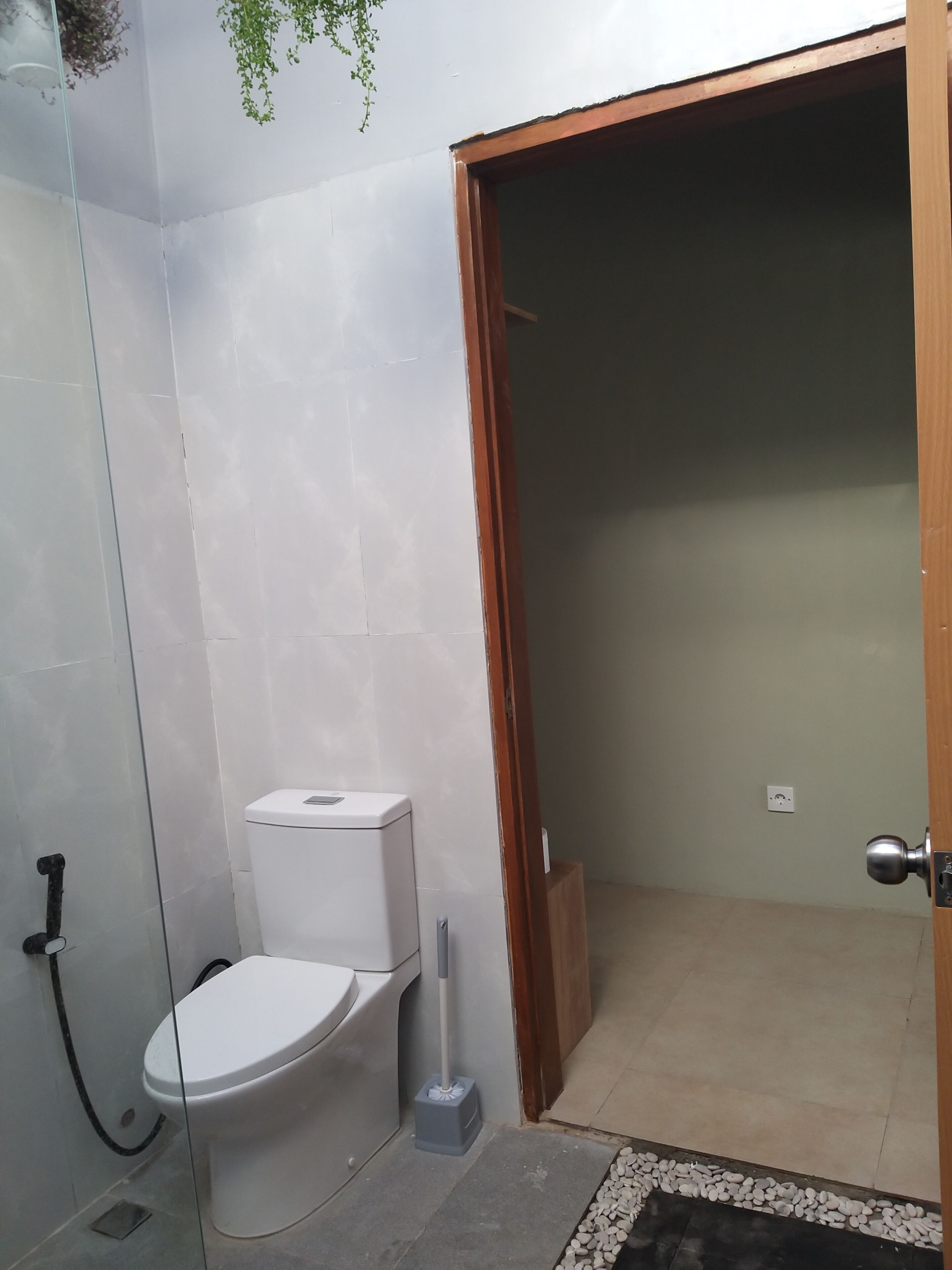 Une salle de bain comprenant des toilettes, une douche et une porte donnant sur une autre pièce.