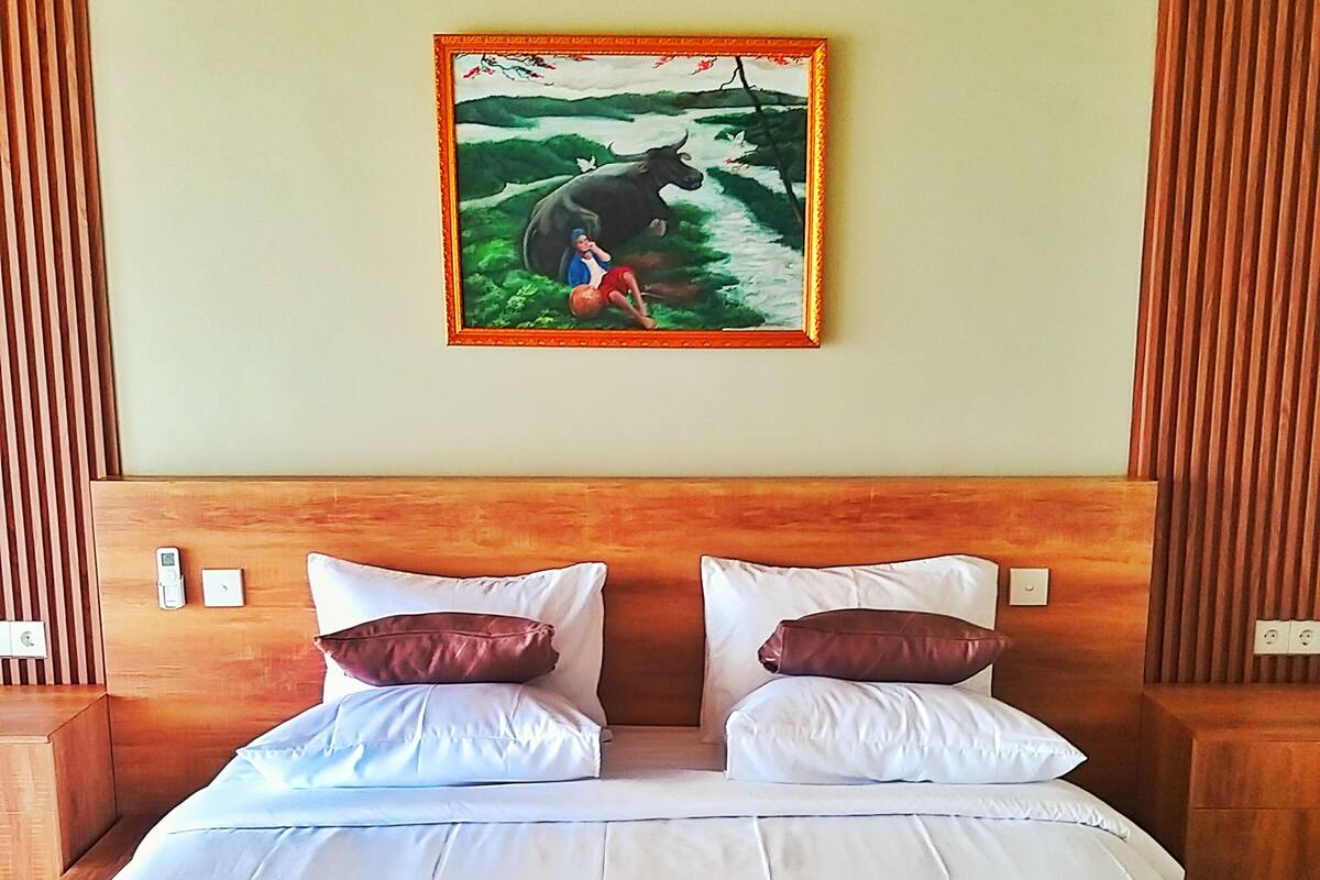 Una cama bien hecha con ropa de cama blanca y marrón, un cabecero de madera y un cuadro de un toro y una persona en la pared de arriba.