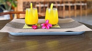 A dining table with two glasses of orange juice, a placemat, and a decorative flower. - Maya Ocean Resort (Kuta)