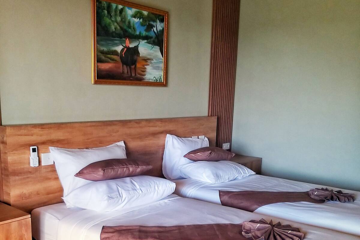 Una cama doble con ropa de cama blanca y marrón, un cabecero de madera y un cuadro de un paisaje en la pared.