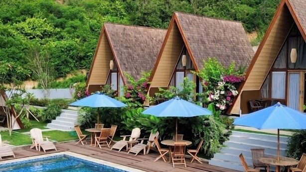 A swimming pool with lounge chairs and umbrellas, surrounded by thatched-roof cottages. - Maya Ocean Resort (Kuta)