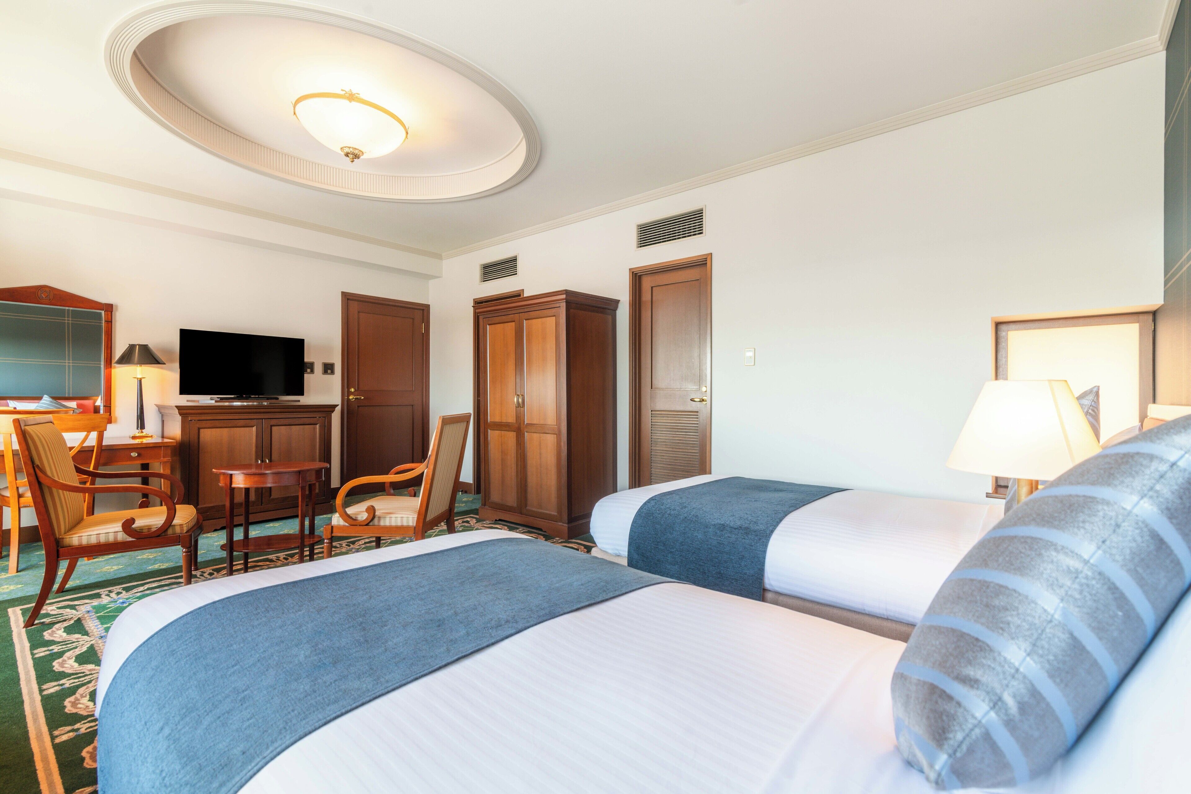 A hotel room with two beds, a desk with a TV, a wardrobe, and a bathroom door.