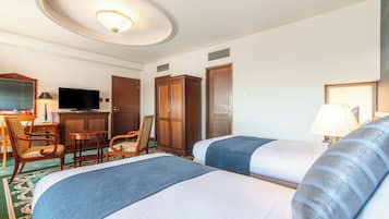 A hotel room with two beds, a desk with a TV, a wardrobe, and a bathroom door.