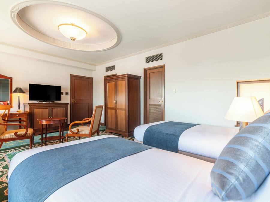 A hotel room with two beds, a desk with a TV, a wardrobe, and a bathroom door.