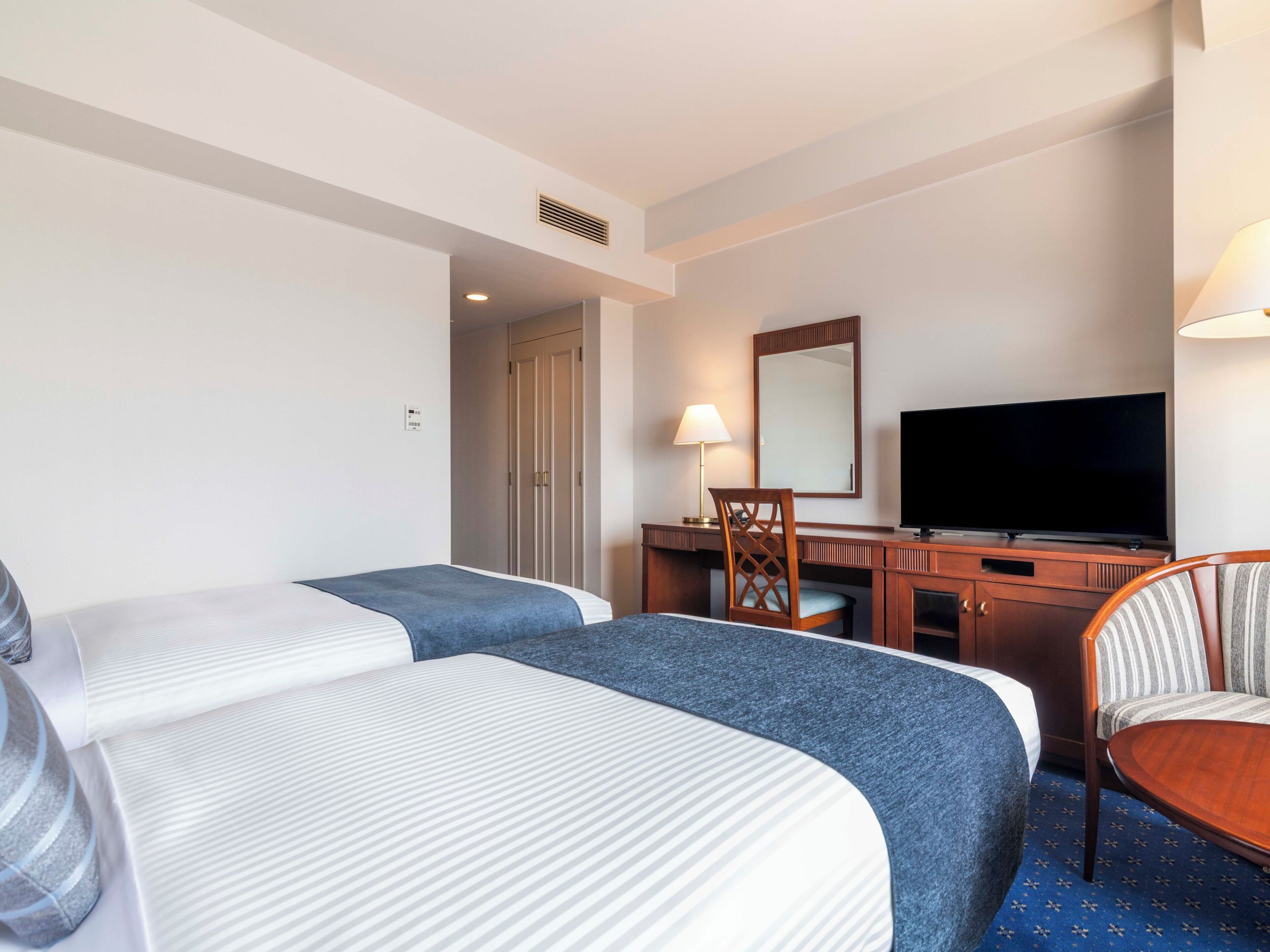 A hotel room with two beds, a desk with a chair, a television, and a large mirror.